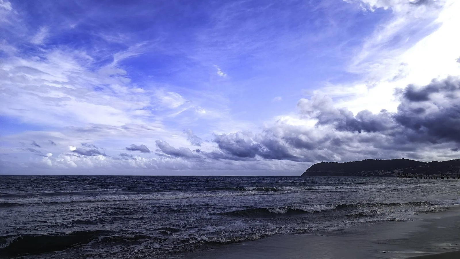 La spiaggia di Alassio fuori stagione, con onde e nuvole sopra Capo Mele